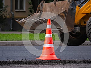 Orange traffic cone on road being repaired. Tractor is driving on background