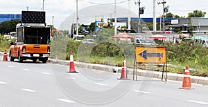 Orange traffic sign with arrow icon and signal cones on highway