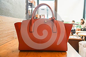 Orange trendy handy leather fashionable women bag on wooden table in coffee cafe