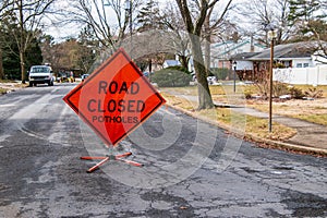Orange triangular road sign on a small suburban street that says Road Closed Potholes. photo