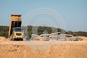 Orange truck unloads sand in the distance next to reinforced concrete slabs