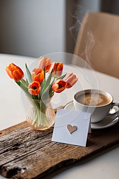 Orange tulips and coffee on rustic wood with blank card and heart decoration conveying a relaxing morning vibe. photo