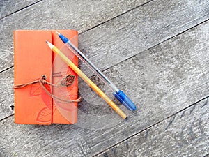 Orange vintage notebook with pen and pencil on wooden table. Creative writing concept. Flat lay top view. Vintage style