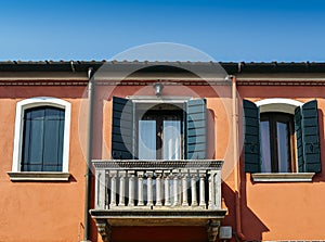 Orange wall of the house with a window with blue shutters and a balcony. photo