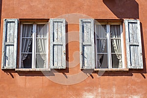 Orange wall with two windows with blue shutters and white curtains