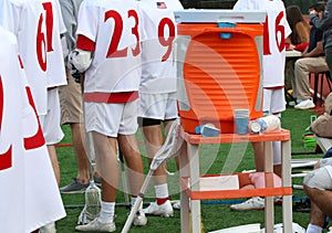 Orange water cooler on a stand by the athletes on the bench of a lacrosse game