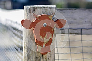 Orange weathered wooden cow head attached to a fence at an entrance to a petting zoo