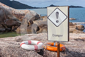 Orange and white life buoys on the rock with danger sign caution