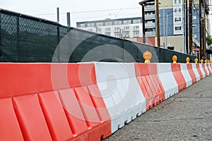 Orange and white plastic Jersey Barriers protect a construction