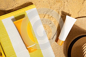 Orange and white tubes of sunscreen on beach next to straw hat and mat. Sun protection on vacation. Top view