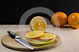 Orange on a wooden round board with sliced slices on a saucer.