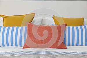 Orange, yellow and blue pillows on white bed at home