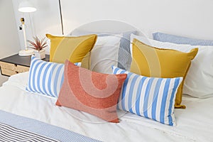 Orange, yellow and blue pillows on white bed at home