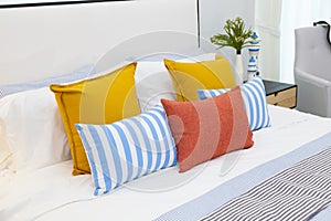 Orange, yellow and blue pillows on white bed at home