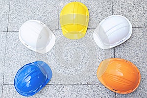 Orange, yellow, blue, white hard safety wear helmet hat in the project at construction site building on concrete floor