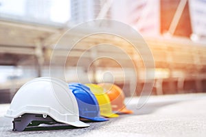 Orange, yellow, blue and white hard safety wear helmet hat in the project at construction site building on concrete floor on city.