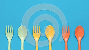 Orange, yellow and green plastic forks and spoons on a blue background. Minimal concept of plastic tableware