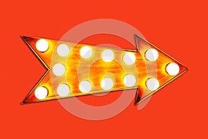 Orange, yellow and red illuminated metallic display golden arrow sign with glowing light bulbs isolated on vivid bright red