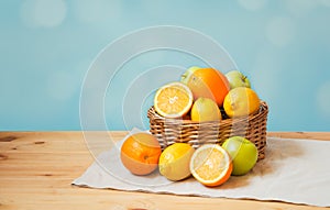 Oranges, apples and lemons in wicker basket and near on wooden table. Selective focus