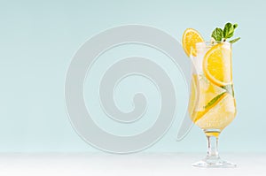 Oranges detox water with sliced orange, ice cubes, green mint in misted wineglass on pastel blue background, white wood board.