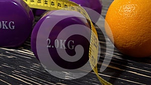 Oranges, juice, dumbbells and measuring tape on wooden background.