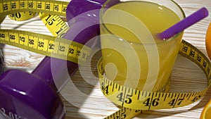 Oranges, juice, dumbbells and measuring tape on wooden background.