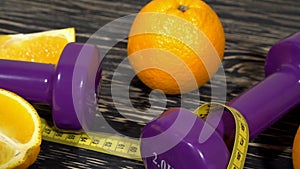 Oranges, juice, dumbbells and measuring tape on wooden background.