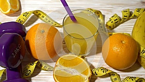 Oranges, juice, dumbbells and measuring tape on wooden background.