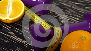 Oranges, juice, dumbbells and measuring tape on wooden background.