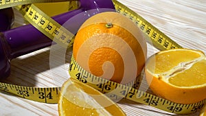 Oranges, juice, dumbbells and measuring tape on wooden background.