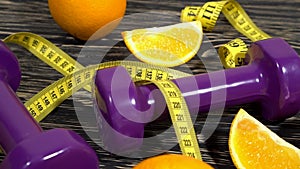 Oranges, juice, dumbbells and measuring tape on wooden background.