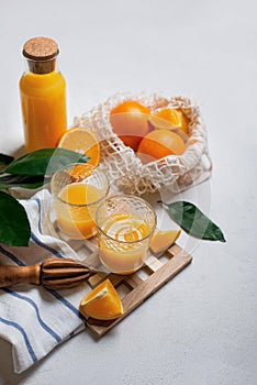 Oranges and juice in glass glasses on a white concrete background