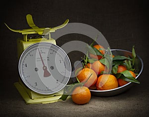 Oranges, tangerines on scales on rustic hessian. Dark, chiaroscuro style still life. Vintage theme.