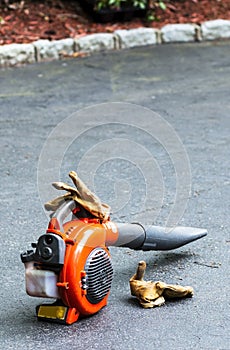 Orangge leaf blower on driveway with landscapers gloves