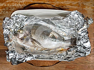 Orata fish baked in foil on old wooden table