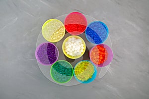 Orbeez toy. Multicolored Hydrogel balls or Water beads in plastic cups on grey background, top view. Flexible gel balls for