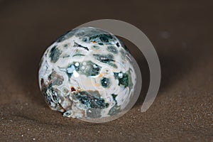 Orbicular Ocean Jasper sphere with crystallized vugs from Madagascar on wet sand  in front of the lake at sunrise