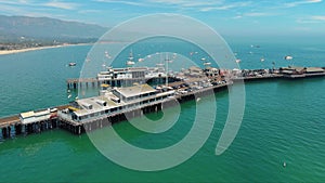 orbit aerial footage of Stearns Wharf Pier with blue ocean water, boats and yachts sailing and people walking and cars driving