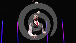 Orbital shot professional circus performer juggling with five white balls against a black studio background amid bright