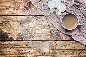 Orchid flower, cup of coffee and beads on a wooden table. Concept romance mood. Copy space and flat lay