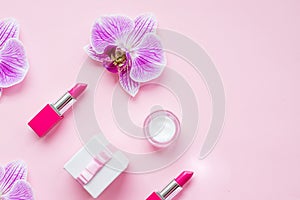 Orchid flowers and decorative cosmetics on pink background. Make up female accessories, stylish flat lay, top view, copy