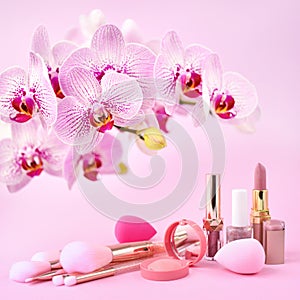 Orchid flowers and decorative cosmetics, sponges  and make-up brushes on a pink background