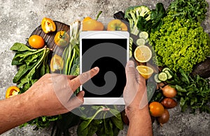 Order Delivery food online concept. Male hands are holding the tablet computer with blank screen over fresh vegetables