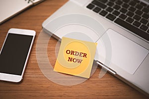 `Order Now` text on post it paper near laptop and smart phone on wood table, Online shopping and Technology marketing concept. Spl