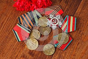 Order of the Patriotic War in St. and Medals for the victory over Germany and two red flower on a table. close up. selective focus