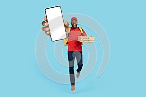 Order Pizza Online. Cheerful Black Delivery Guy Jumping And Showing Blank Smartphone