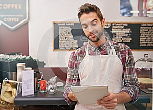 Ordering new stock online. a young male barista using his tablet in a coffee shop.