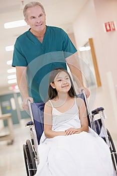 An Orderly Pushing A Little Girl In A Wheelchair