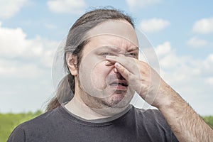 An ordinary middle-aged adult man with long tail hair pinches his nose with two fingers from a bad smell.