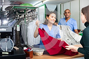 Ordinary woman and man working with client in modern laundry